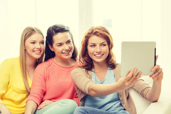 Three smiling teenage girls with tablet pc at home