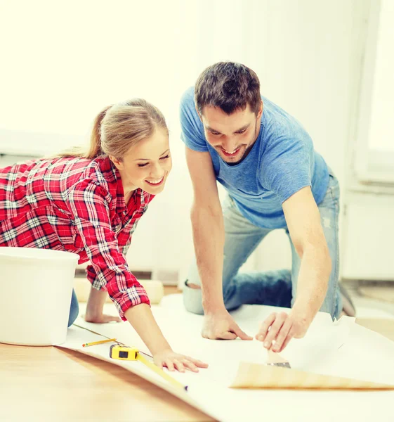 Smiling couple smearing wallpaper with glue