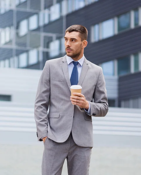 Young serious businessman with paper cup outdoors