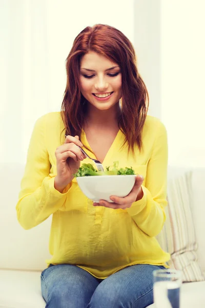 Smiling young woman with green salad at home