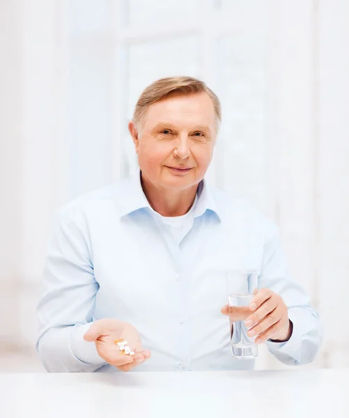 Old man with pills ang glass of water