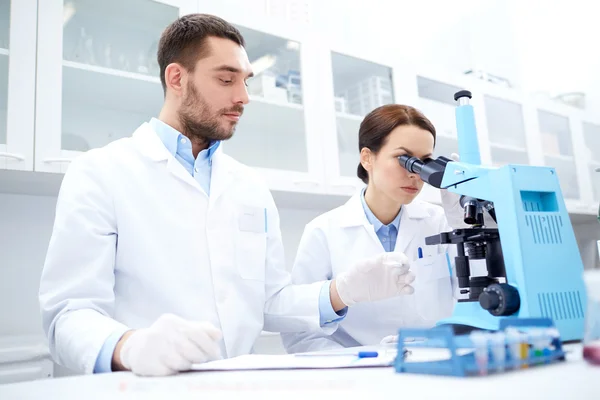 Scientists with clipboard and microscope in lab