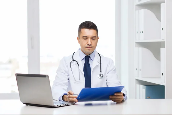 Male doctor with clipboard and laptop in office