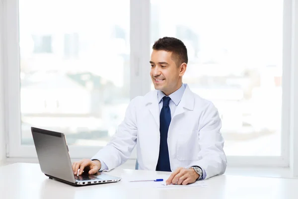 Smiling male doctor with laptop in medical office