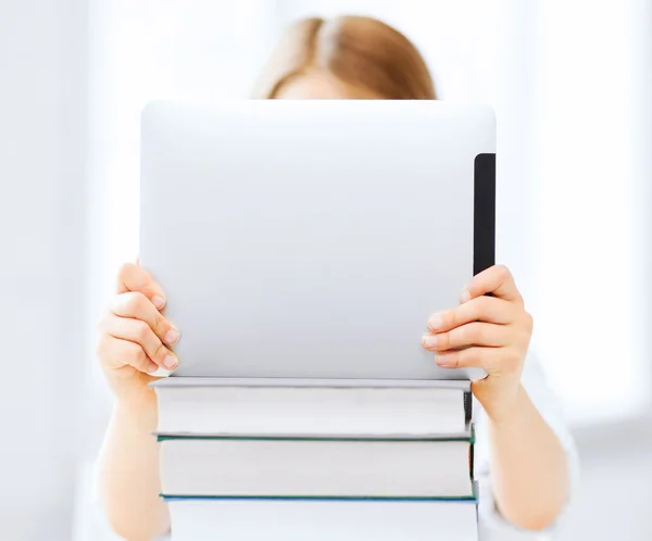 Girl hiding behind tablet pc and books at school