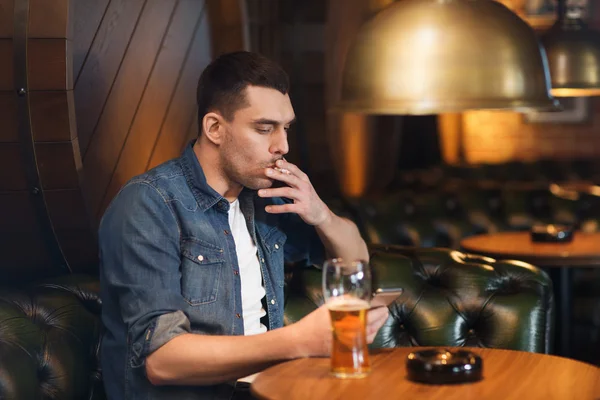 Man drinking beer and smoking cigarette at bar