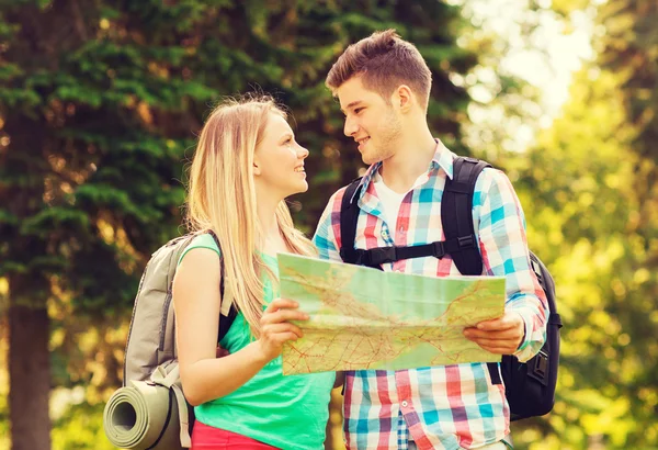 Smiling couple with map and backpacks in forest