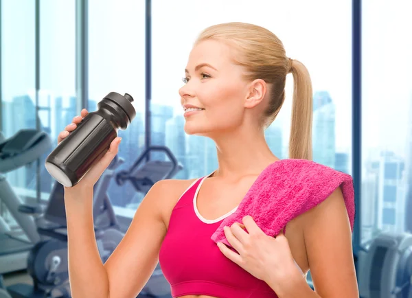 Happy woman drinking water from bottle in gym