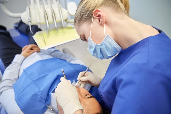 Female dentist in mask checking male patient teeth