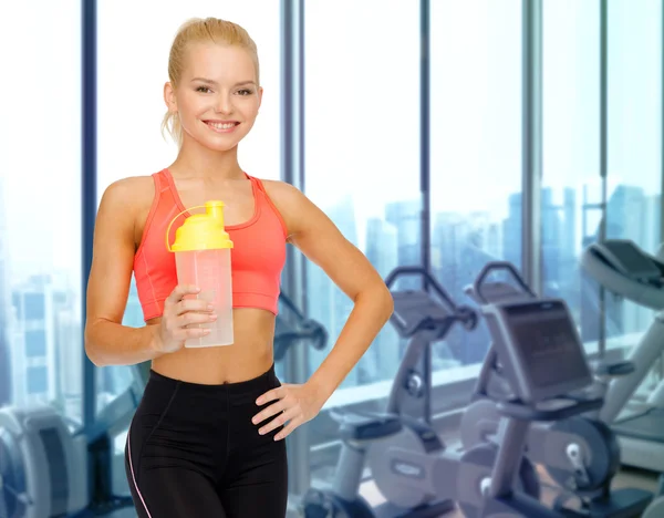 Happy woman with protein shake bottle in gym