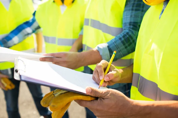 Close up of builders in vests writing to clipboard