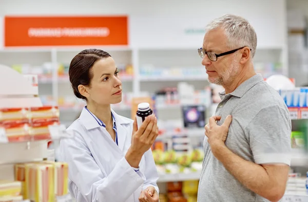Pharmacist showing drug to senior man at pharmacy