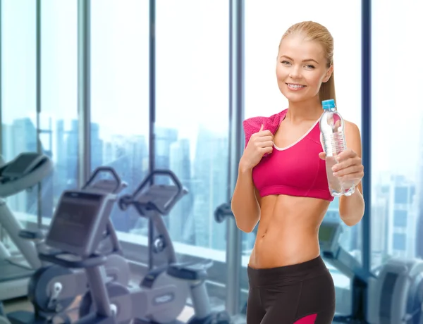 Happy woman with bottle of water and towel in gym
