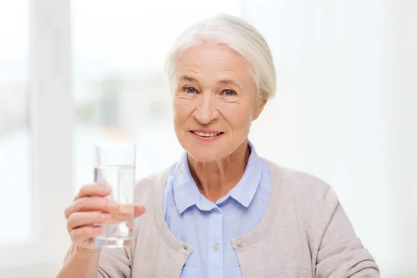 Happy senior woman with glass of water at home