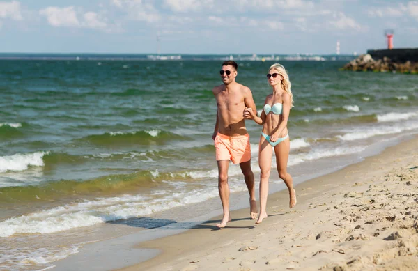 Happy couple in swimwear running on summer beach