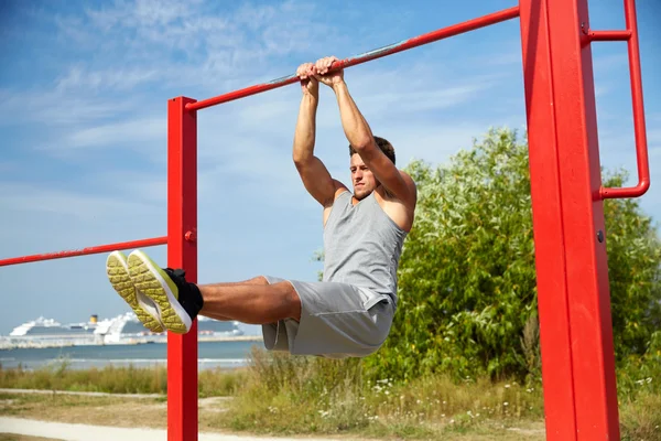 Young man exercising on horizontal bar outdoors
