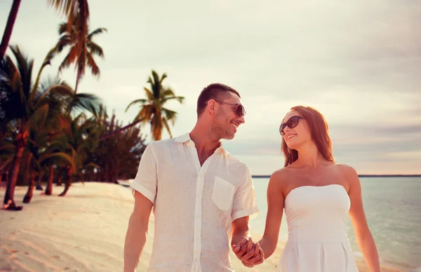Smiling couple in sunglasses walking on beach