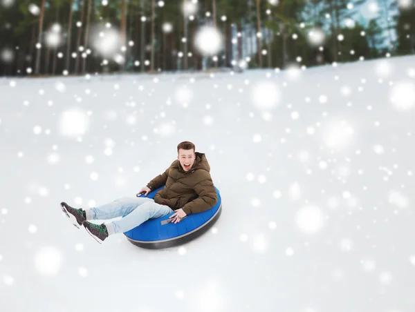 Happy young man sliding down on snow tube