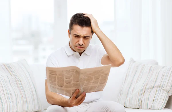 Sad man reading newspaper at home