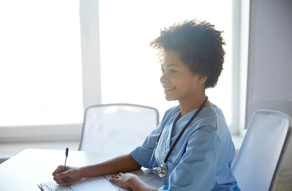 Happy female doctor or nurse writing at hospital