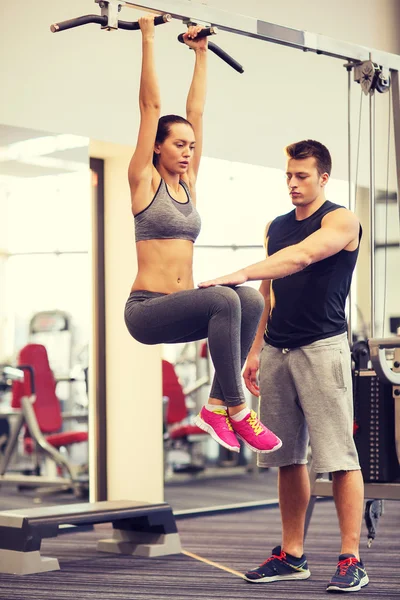 Young woman with trainer doing leg raises in gym