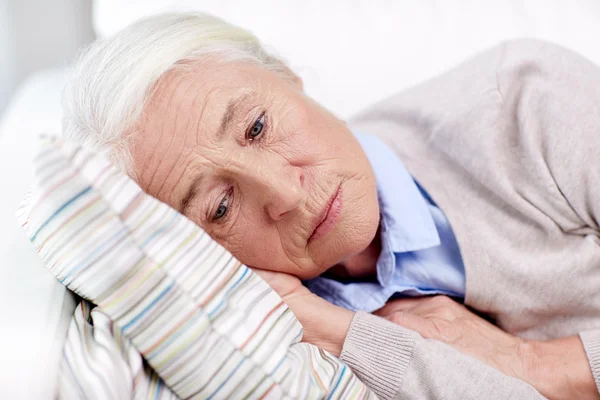 Sad senior woman lying on pillow at home