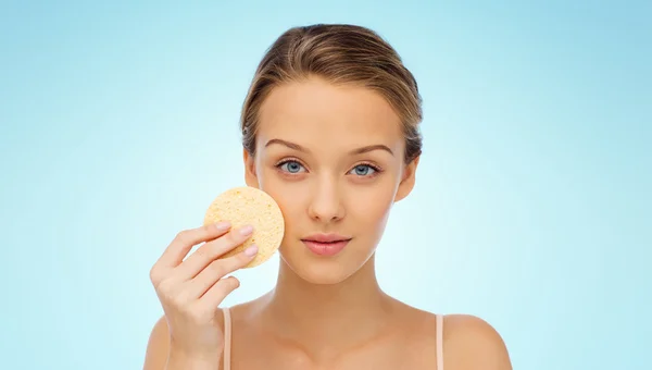 Young woman cleaning face with exfoliating sponge