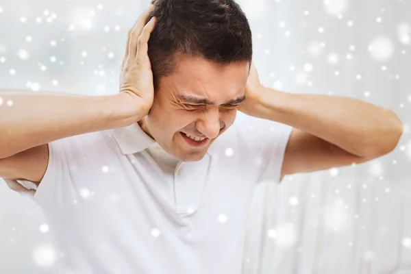 Unhappy man closing his ears by hands at home