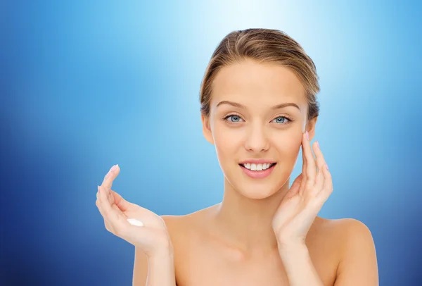Happy young woman applying cream to her face