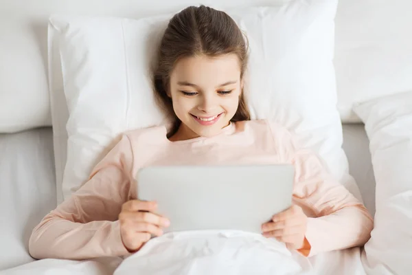 Happy girl lying in bed with tablet pc at home