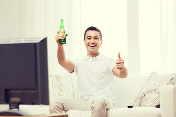 Smiling man watching tv and drinking beer at home