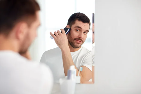 Man shaving beard with trimmer at bathroom