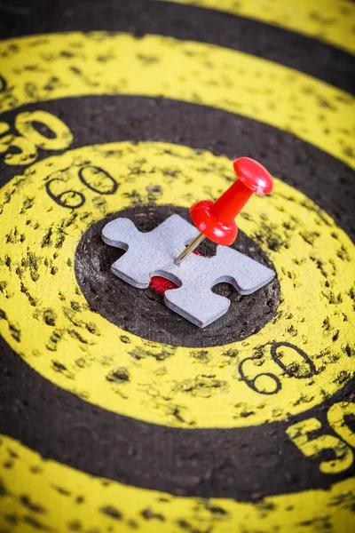 Red pin stuck to man shape jigsaw puzzle piece on old target board