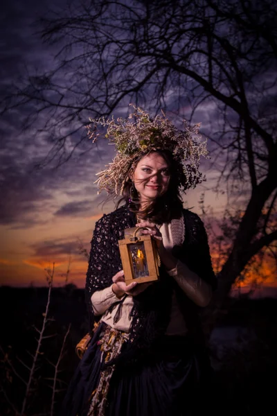 Beautiful young witch with lamp in her hand in sunset