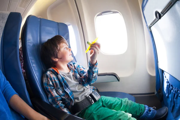 Boy with toy plane sits  by airplane window