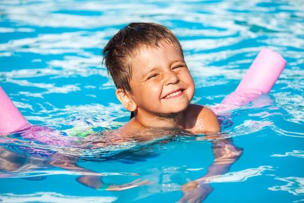 Boy learning to swim with pool noodle