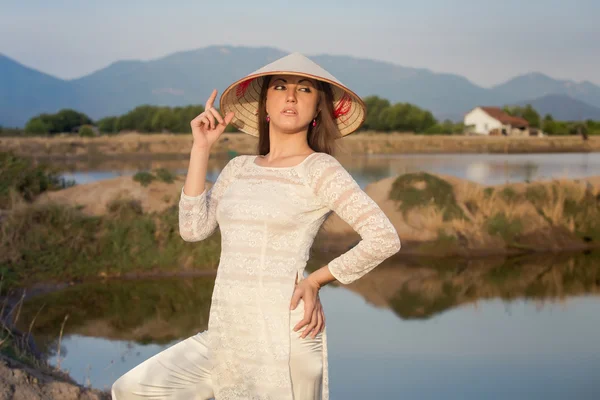 Blonde girl in Vietnamese dress smiles against country lakes