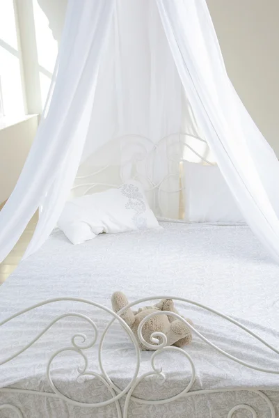 White bed with a baldachin and bruin