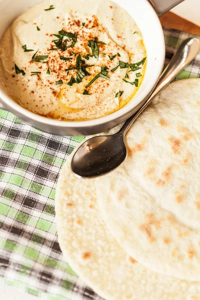 A bowl of creamy hummus with olive oil and pita chips.