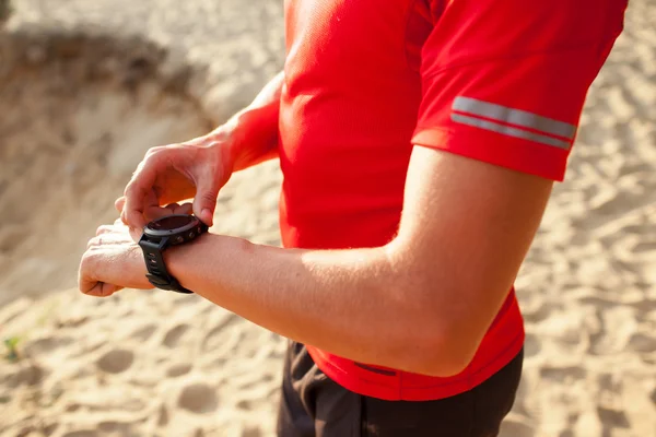 Runner on mountain trail looking at sportwatch smart watch, chec