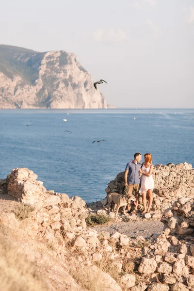 Couple of guys playing with their dog on the mountain near ocean. Romantic time in nature with beautiful view.