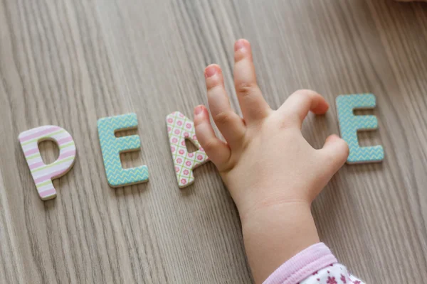 Child is Writing Word Peace From Colourful Toy Letters