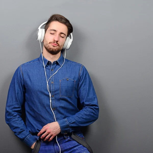 Young man leaned on the wall enjoying music against gray backgro