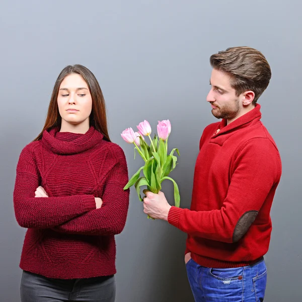 Portrait of unhappy young woman getting flowers from man she doe