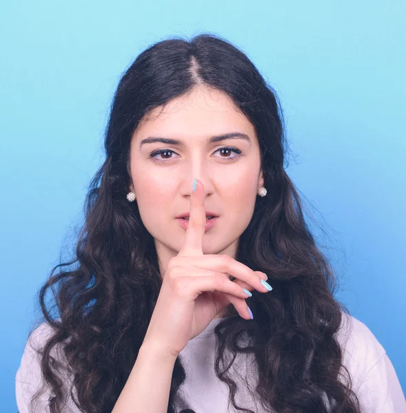 Portrait of girl with gesture for silence against blue backgroun