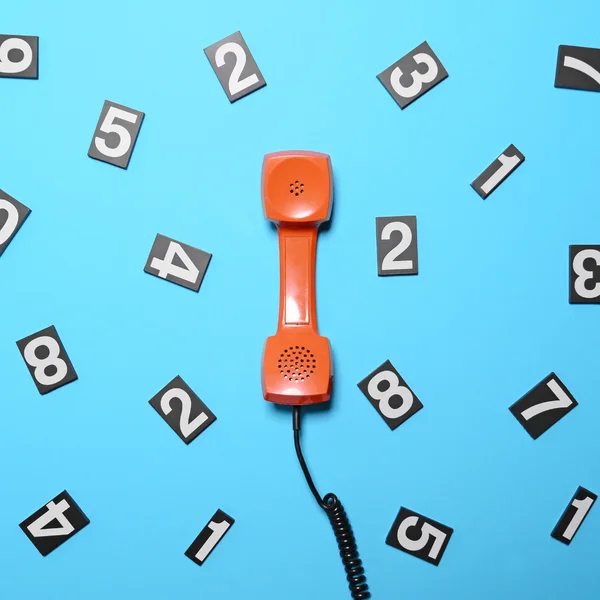 Retro orange telephone tube with numbers around it on blue backg