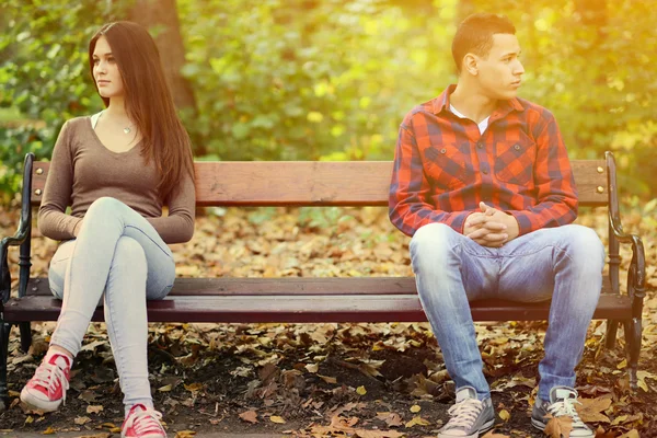 Young couple in quarrel sitting on bench in park