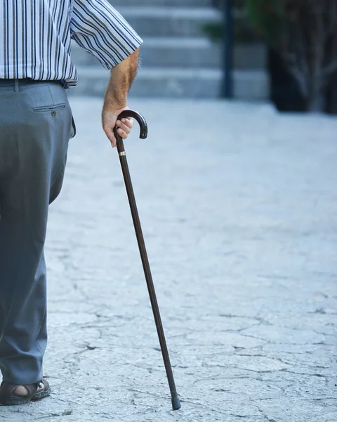 Old man walking with his hands on a wooden walking stick