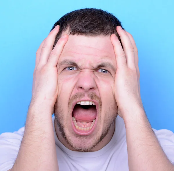 Portrait of angry man screaming and pulling hair against blue ba