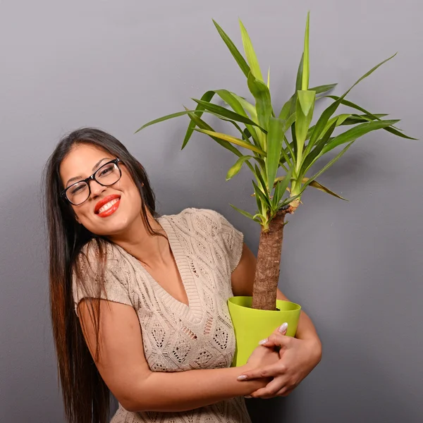 Beautiful happy woman holding plant in vase against gray backgro